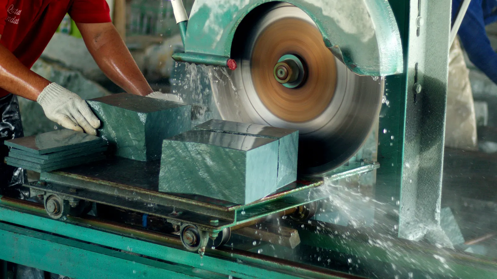 Factory technician wet-cutting a raw Sukabumi Green Stone block on a diamond-blade saw